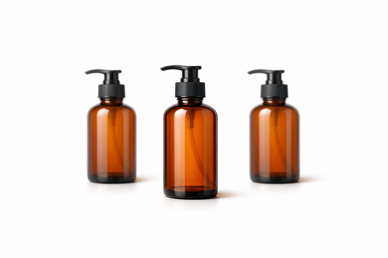 Three amber glass bottles with black pump dispensers on pure white background — clean product photography